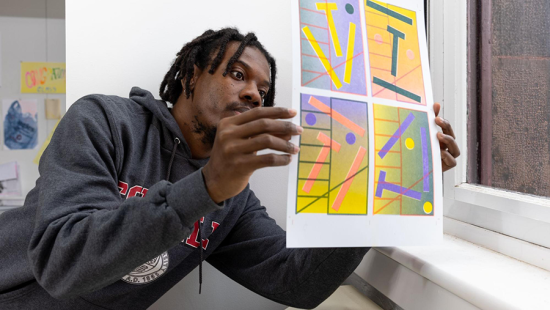 Student examines brightly colored printed poster near a window.