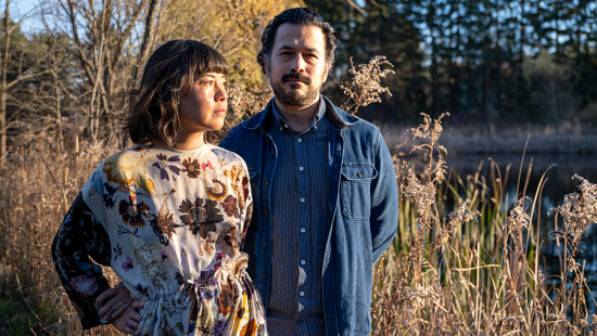 A man and woman standing in a wooded field at sunset