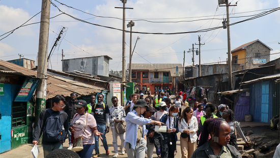 Students walk with local community members down a street between homes and shops