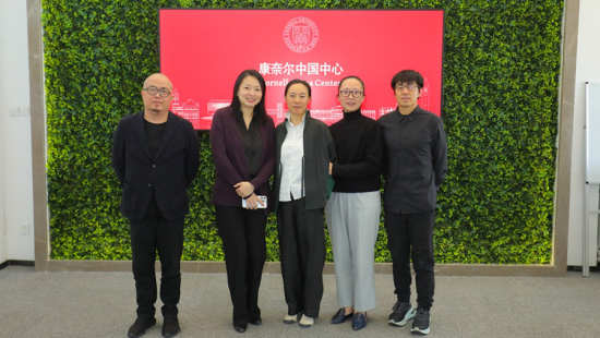 Five people formally dressed lined up in front of a red sign and greenery background.