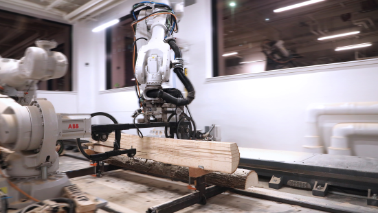 A large robotic arm handling a piece of wood in a white room with windows.
