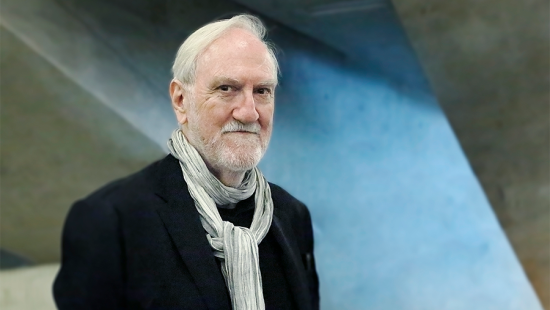 Older man with white hair wearing a black sport coat and white scarf