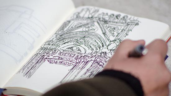 An open notebook with a hand sketching with a pen.
