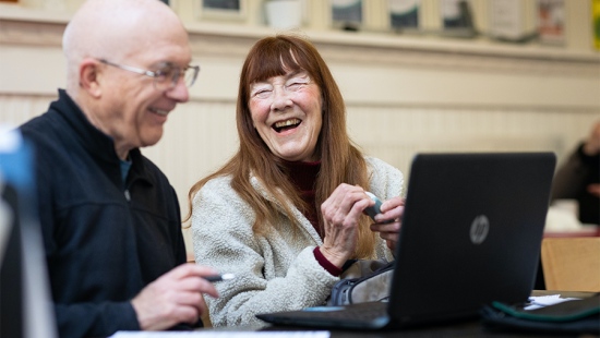 older couple laughing in front of an open laptop