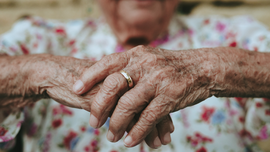 Hands of an elderly person wearing a wedding band crossed in front
