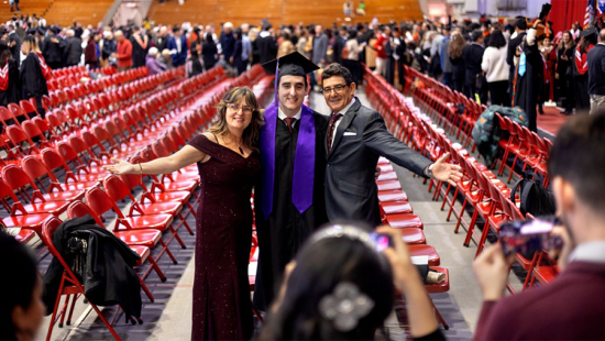 Student in cap and gown flank by parents posing for a celebratory photograph