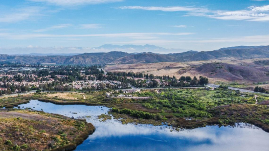 A wetland area with mountains and a bright blue cloudy sky.