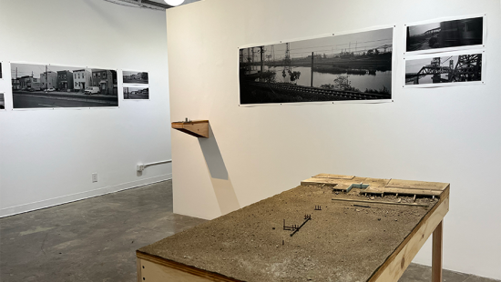 Gallery space with black and white images mounted on the walls and a table displaying a model