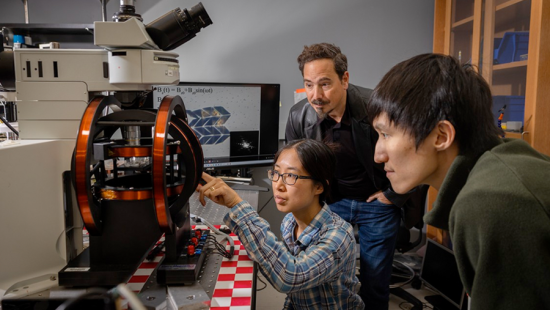 Three people looking at some equipment that resembles a high-tech microscope.