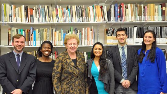 An older woman poses for a photo with five college students.