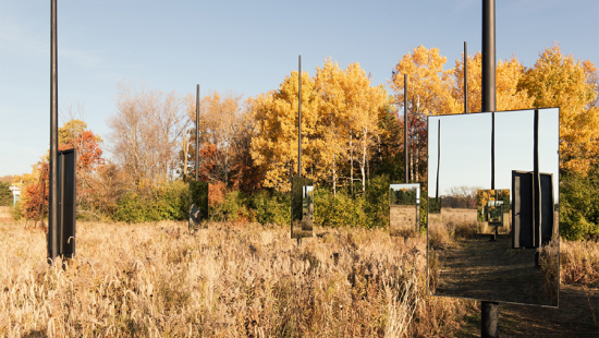 Mirrors mounted on wooden poles reflecting a grassy brown field