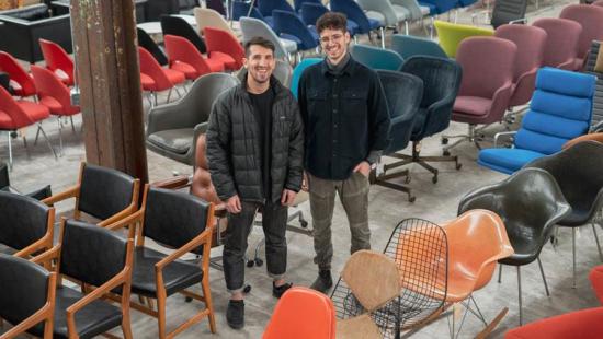 Two men standing on a warehouse floor surrounded by brightly colored furniture