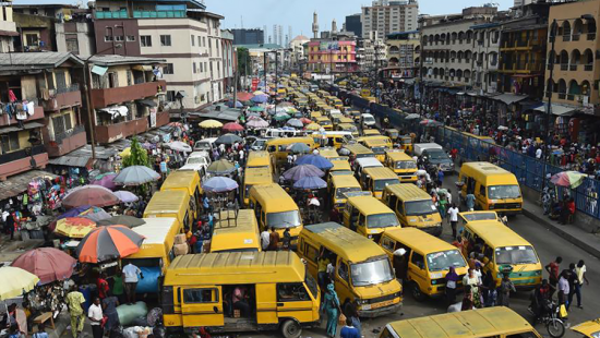 Busy street filled with yellow vehicles, umbrellas, people and buildings.