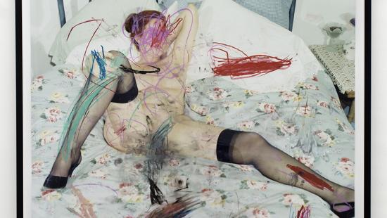 A painting of a woman, wearing nothing but stockings and heels, lying on a bed with a blue floral blanket on top. Artfully placed scribbles cover various parts of her body.