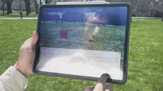 Two hand holding a digital tablet with an augmented reality image over a grassy lawn