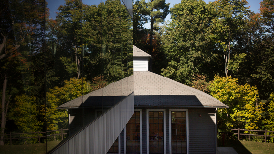 A building façade of windows and another building surrounded by trees and a blue sky in the background.