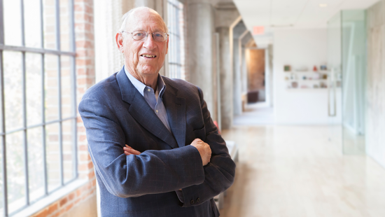 A man wearing a blue suit standing with his arms folded across his chest.