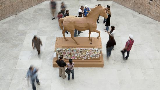 People standing around a wooden horse with notes attached to it's base.