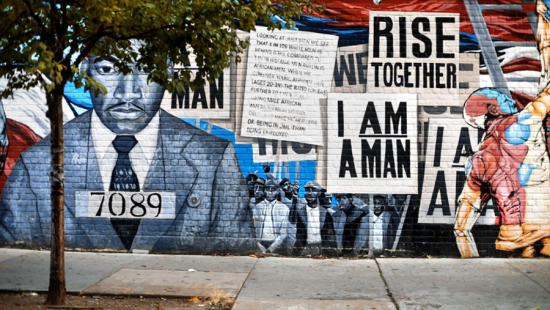 A mural with a man wearing a suit with a number around his neck on a brick building.