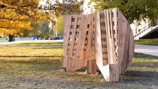 Slatted and perforated wooden structure in a park-like setting.
