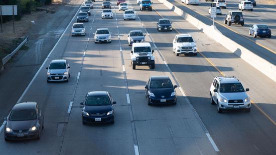 A dozen automobiles approaching on a four lane highway viewed from above.