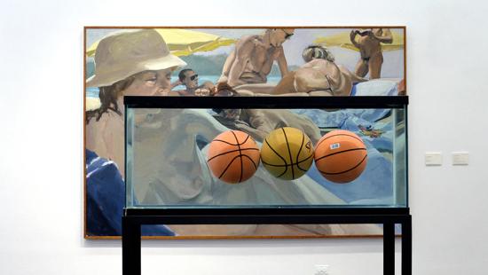 Three basketballs float in an aquarium with a painting of nudes behind it.