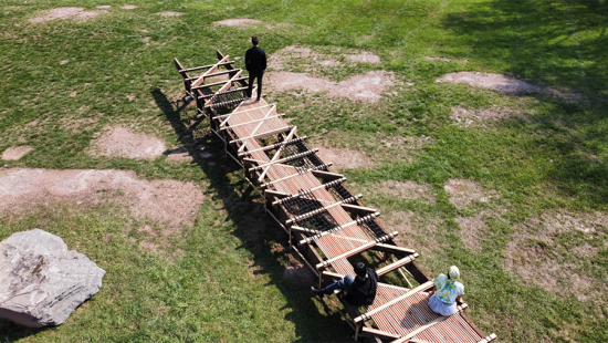 Wooden structure on grass with three people sitting or standing on  it.