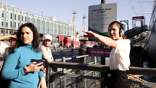 Woman speaking with students at the sea port and pointing forward