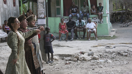 Three people in costumes are watched by children and adults in a street.