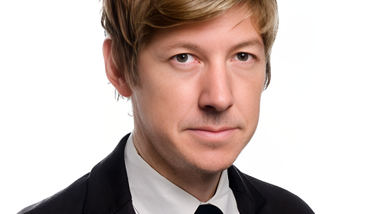 Blonde man wearing a black suit and tie with white shirt