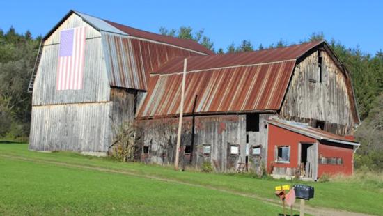 Old barn with rusted metal roof on a grassy hillside.