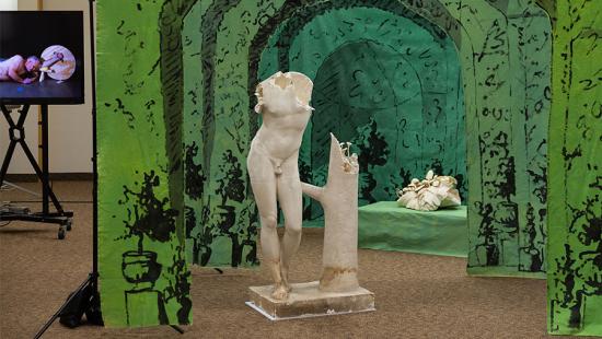 plaster cast sculpture of human torso and legs in front of hung green material