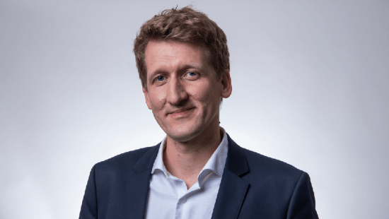 A person with short hair, wearing a dark blue suit jacket.