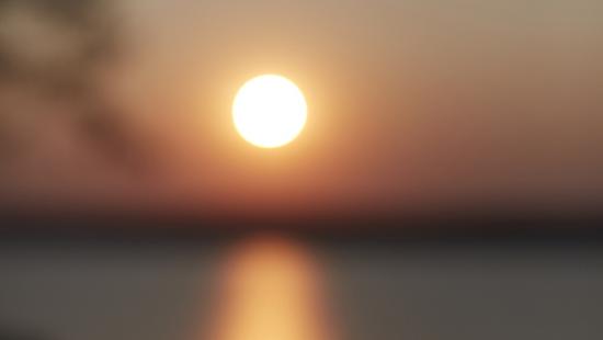 A sunset over a body of water with an out of focus tree.