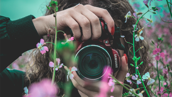 woman with a camera up to her eye obscured by some flowers