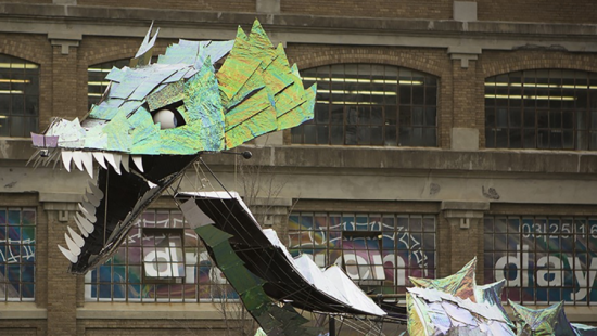 A silvery and green dragon head with white eyes in front of a building.