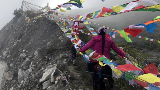 person wearing pink jacket following rows of prayer flags along a mountain path