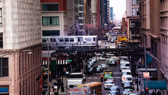 A city corridor with traffic congestion and a train overhead.