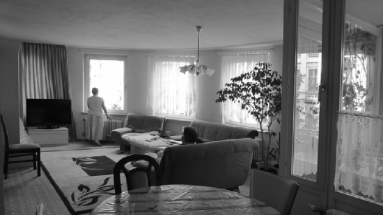 Black and white view of a living room with two occupants, one seated and one at the window
