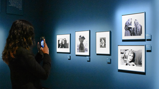 Student taking a photograph of framed images hanging on a blue wall.