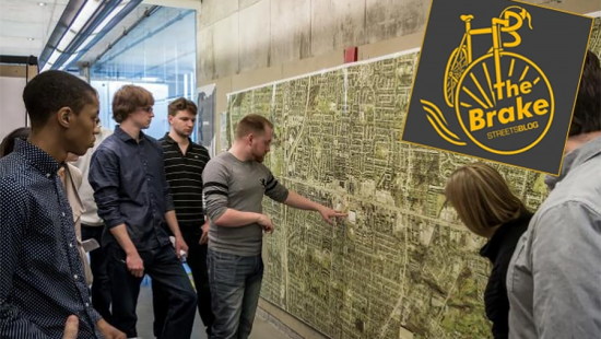 People gathered around a large map of city streets pinned up on a wall.