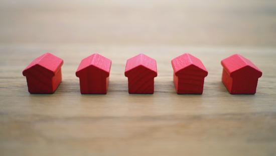 Five miniature, red house shapes in a row on a wood surface.