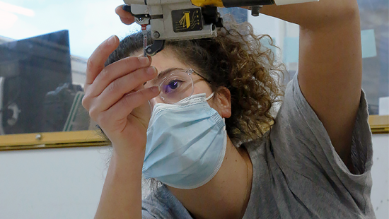 Student wearing surgical mask and glasses adjusting machinery.