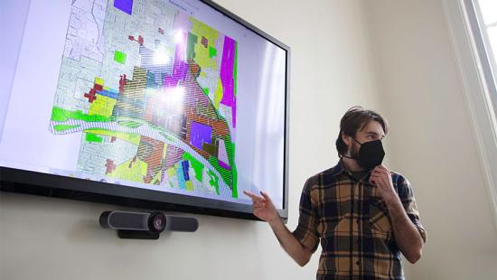 Student gestures at a screen displaying a multi-colored city map