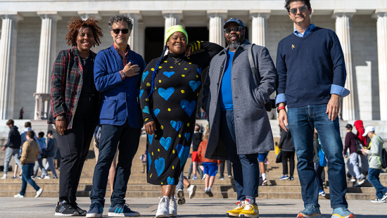 Five adults standing on the steps in front of a large white marble building