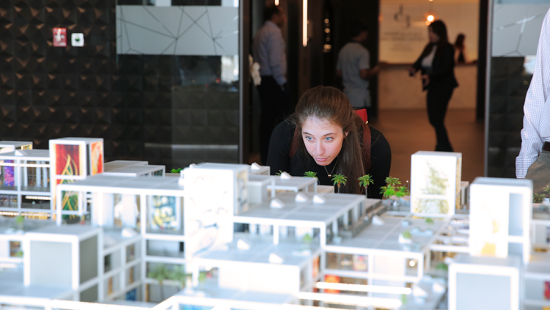 Woman examines architectural model of an urban streetscape.