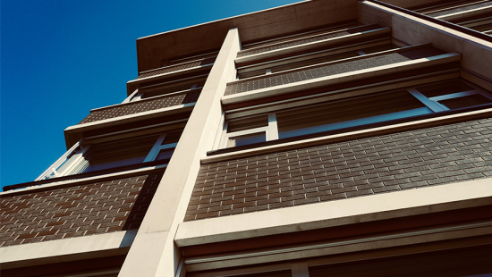 A school building from the ground, looking up past several floors of bricks and windows backed by the blue sky.