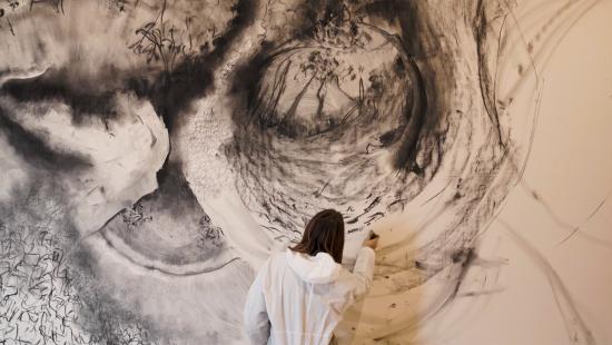A person drawing on a large white wall with black chalk.