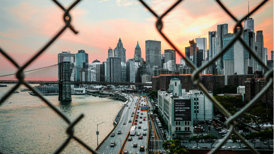 a city skyline as seen though a broken chain link fence.