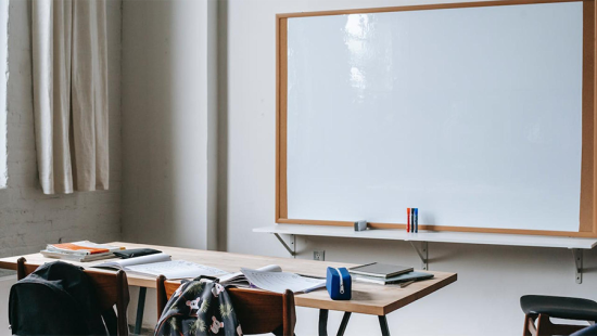Desk covered with student supplies in front of a blank white board